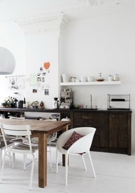 a Scandinavian kitchen with dark-stained reclaimed wood cabinets, a stained table and mismatching chairs, an open shelf
