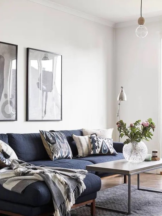 a Scandinavian living room with a navy sectional sofa, a coffee table, black and white artwork and a floor lamp plus some blooms