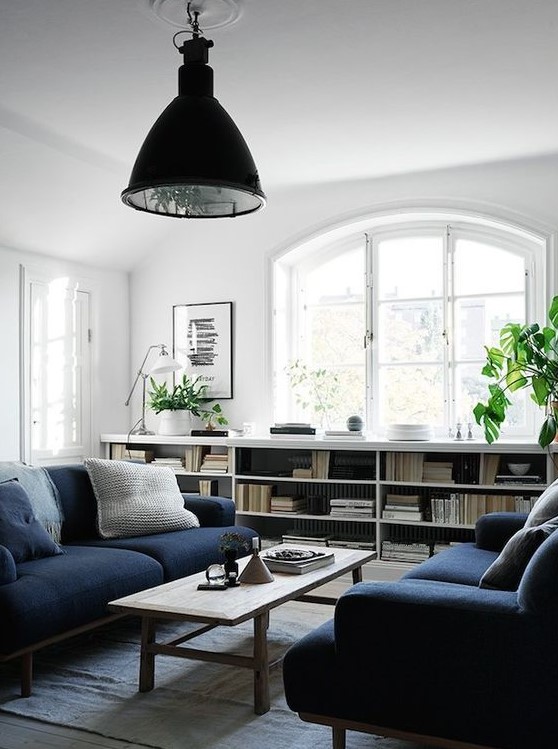 a Scandinavian living room with bookshelves, navy sofas, a coffee table, potted plants and a black pendant lamp