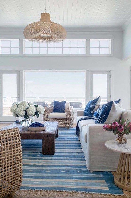 a beach living room with cool views, white upholstered and rattan furniture, a striped rug and printed pillows