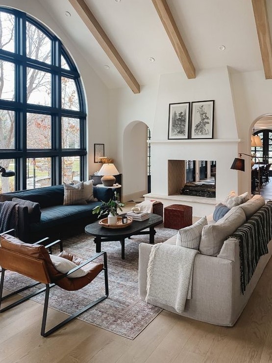 a beautiful and refined living room with an arched French window, a navy and a grey sofa, a leather chair and a coffee table and some lamps