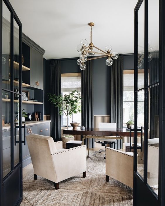 a beautiful soot home office with cabinetry, a stained desk, creamy chairs, a chic chandelier and greenery