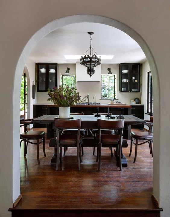 a black kitchen with a kitchen island, a dark-stained dining table and brown leather chairs, a vintage chandelier