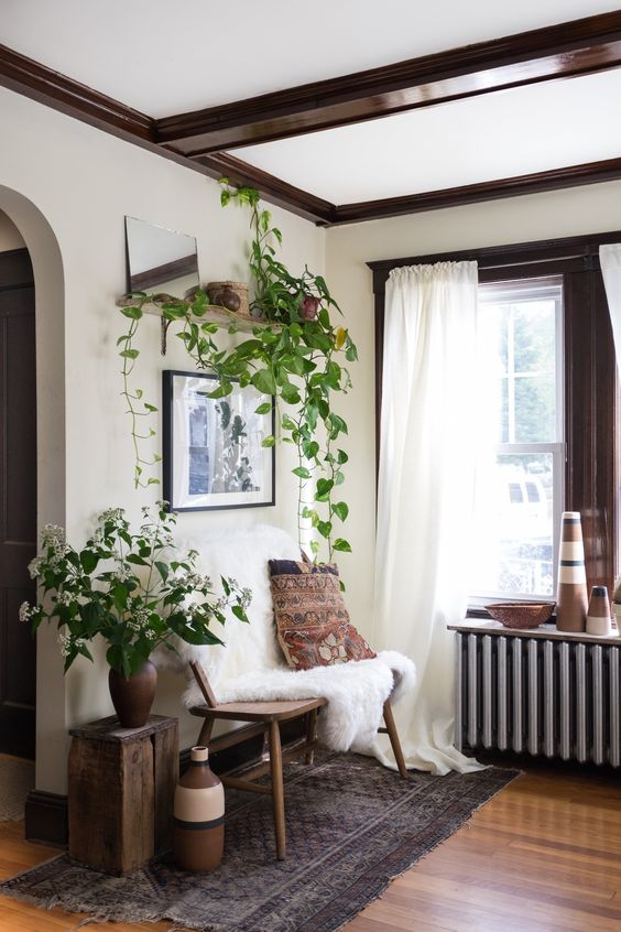 a boho space with dark-stained wooden beams, a wooden bench and a stool, vases and potted greenery