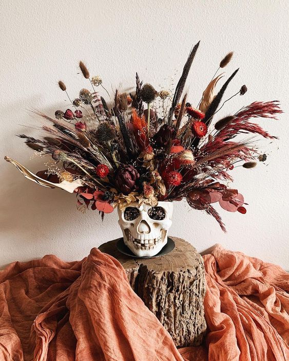 a bold Halloween arrangement in a skull, with dried grasses and blooms plus leaves is a catchy Halloween decoration