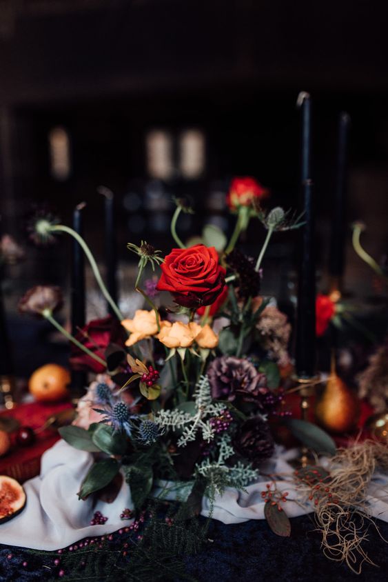 a bold Halloween centerpiece of orange, red and purple blooms, greenery and thistles is a catchy arrangement