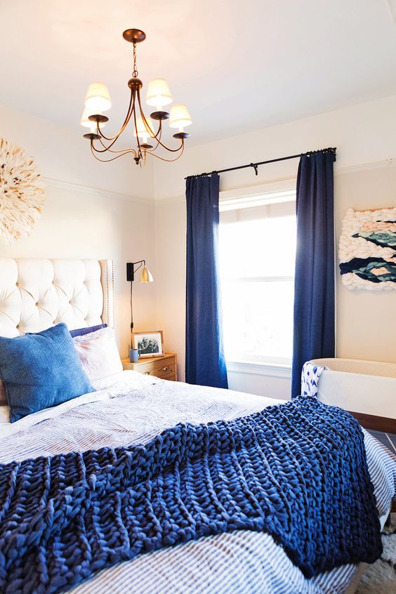 a-bold-bedroom-with-a-white-bed-navy-and-white-bedding-navy-curtains-a-macrame-artwork-and-a-crib.jpg