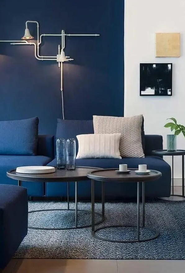 a bright modern living room with navy walls, navy sofas, black side tables and cool art, unique industrial-inspired sconces