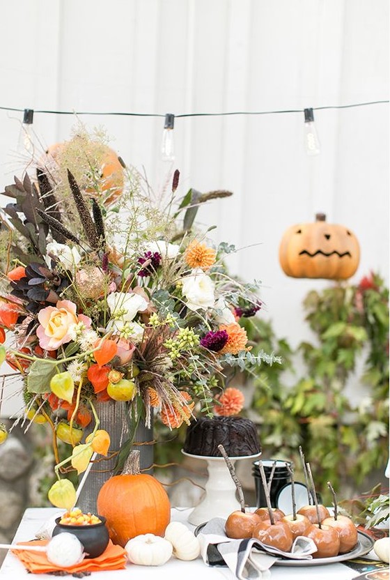 a bright rustic Halloween centerpiece with fresh peachy, orange and dried blooms, dark and usual foliage and greenery