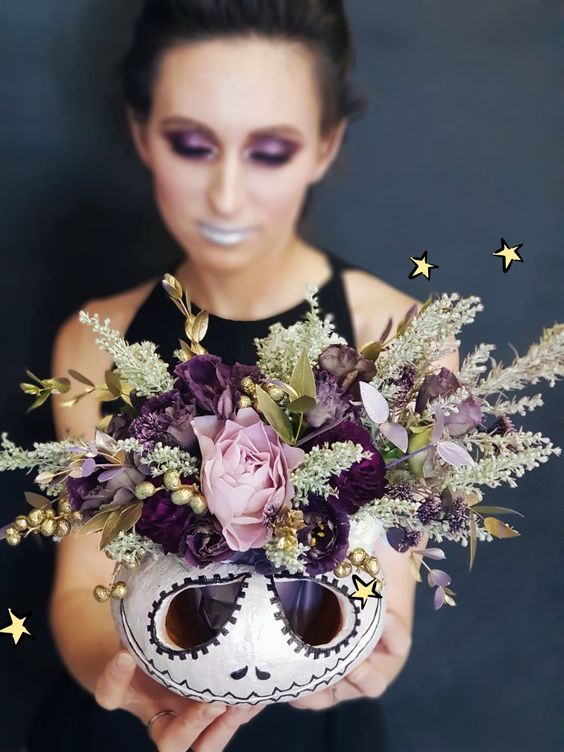 a catchy Halloween decoration of a white carved pumpkin, lilac and purple blooms, gilded foliage and herbs