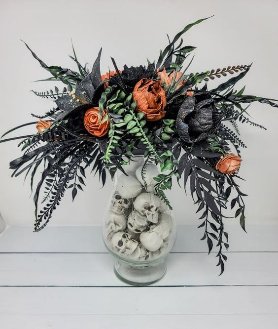 a catchy Halloween flower arrangement in orange and black, with green and black leaves, with skulls in the vase