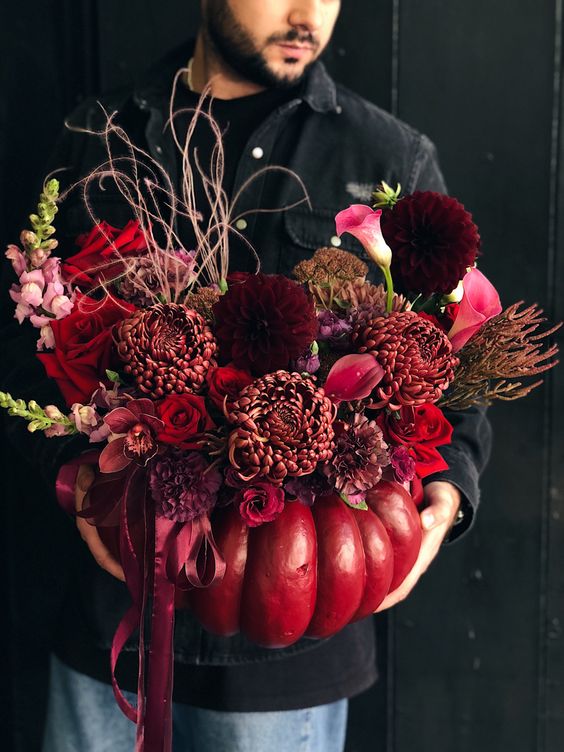 a catchy and bold Halloween decoration of a red pumpkin, burgundy roses, callas, chrysanthemums, twigs and herbs