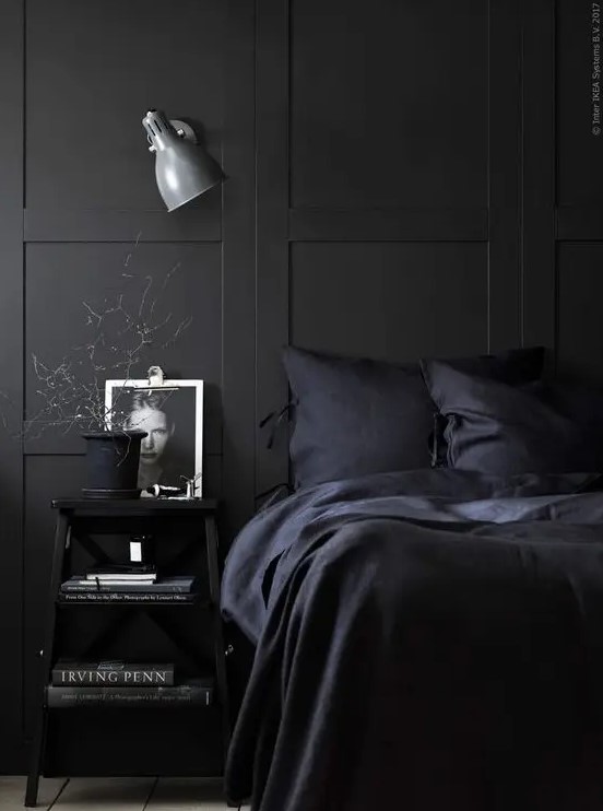 a chic Nordic moody bedroom with black paneling, navy bedding and black furniture plus a sconce