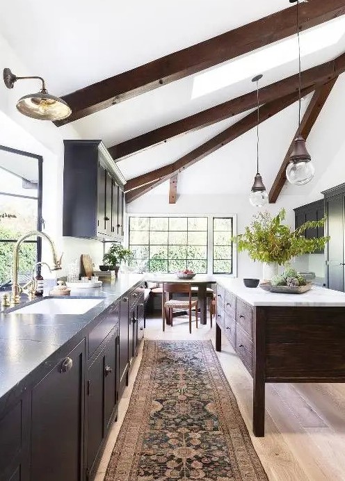 a chic modern farmhouse kitchen with a light-stained floor, dark wooden beams and a kitchen island that dominate over the space