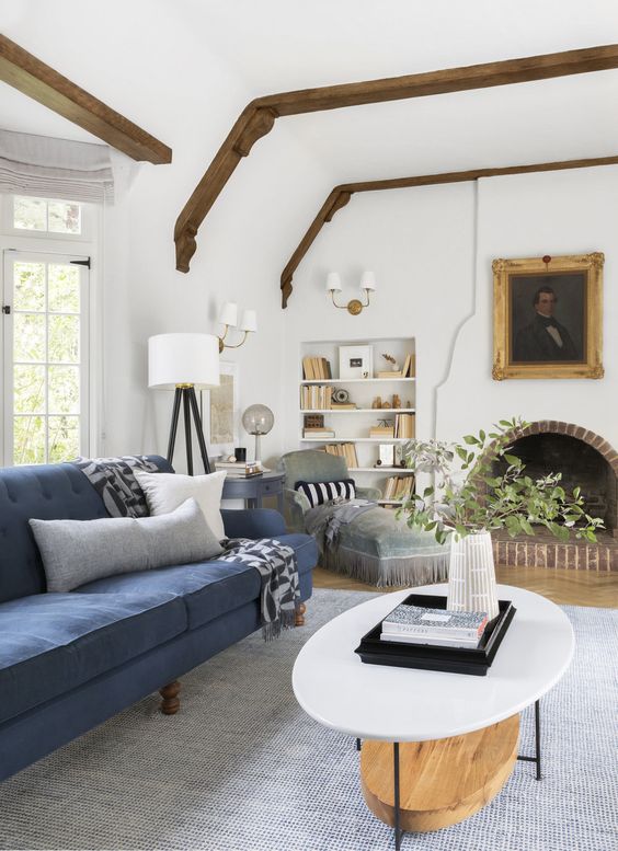 a chic modern living room with an arched fireplace, built-in shelves, a navy sofa, a grey daybed and a tiered coffee table