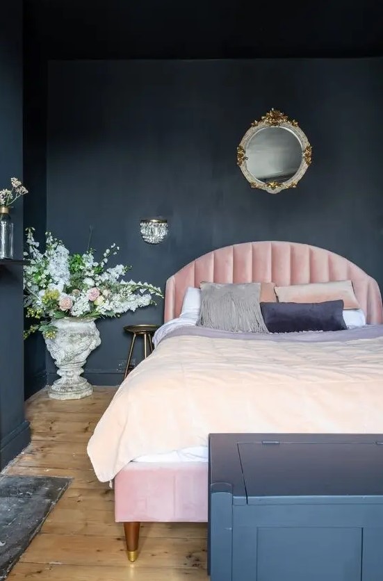 a chic moody bedroom with soot walls and a chest for storage, a light pink bed, refined lighting and blooms
