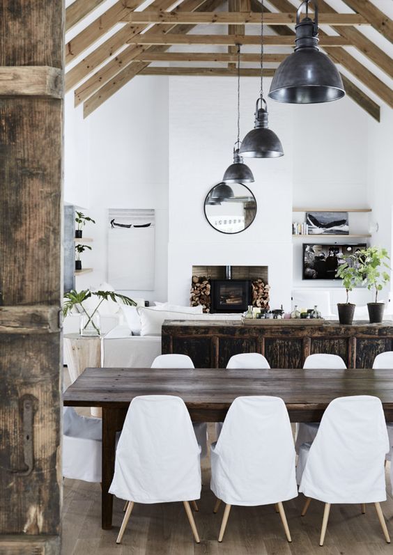 a chic open layout with a dark-stained cabinet, a dark-stained dining table, white seating furniture and industrial lamps