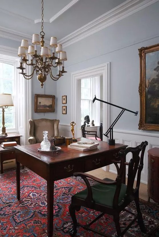 a chic vintage home office with a rich-stained desk, a green chair and a taupe one, a chic chandelier and a printed rug