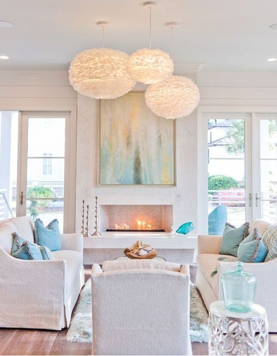 a chic white beach living room with aqua and turquoise touches, fluffy pendant lamps, a fireplace