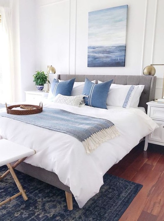 a-coastal-bedroom-with-a-grey-upholstered-bed-blue-and-white-printed-textiles-a-sea-artwork-a-stool-and-potted-plants.jpg