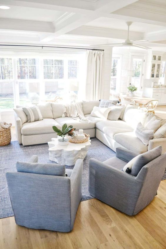 a coastal living room with a white sectional, blue chairs, a matching rug, a coffee table and a basket