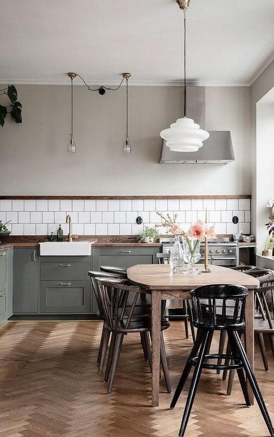 a contemporary Scandi kitchen with a white tile backsplash, dark-stained countertops, a herringbone wooden floor, a light-stained table, dark-stained chairs and a black chair