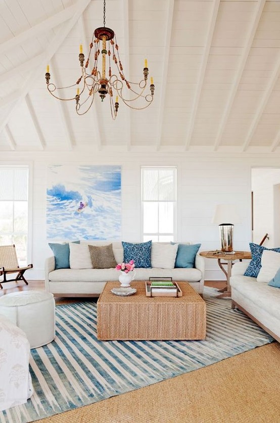 a cozy coastal living room with a cork coffee table, a striped rug, blue pillows and white furniture