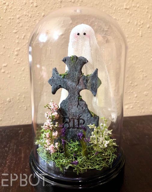 a creative Halloween cloche with hay, blooms, a tombstone and a ghost is a cool decoration to rock