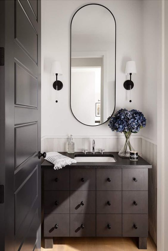 a dark-stained bathroom vanity with multiple drawers, an oval mirror and sconces is a cool idea to add a refined touch to the space