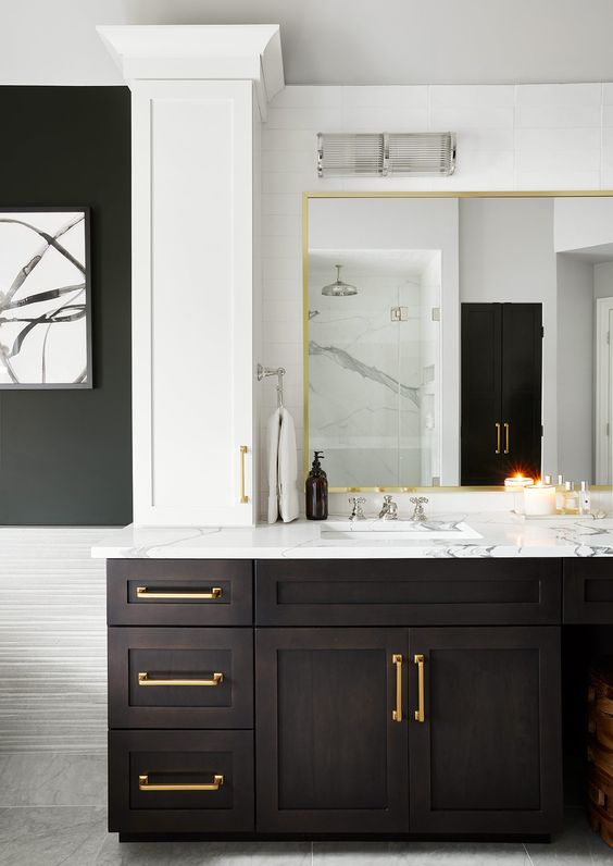 a dramatic bathroom with a large dark-stained vanity with a mirror in a gilded frame, a white stone countertop and gold touches