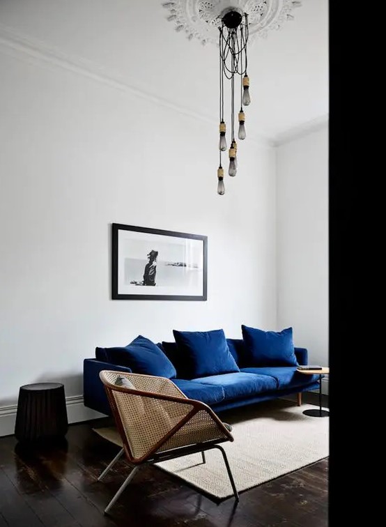 a dreamy living room done in contrasting colors, with a navy sofa, cane chairs, round side tables and bulbs hanging from the ceiling medallion