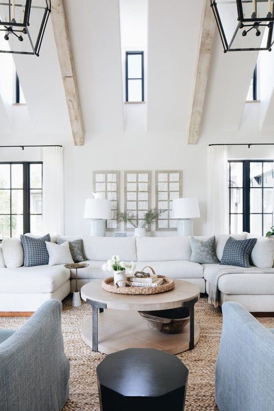 a farmhouse living room with a neutral sectional, pale blue chairs and printed pillows, a tiered coffee table