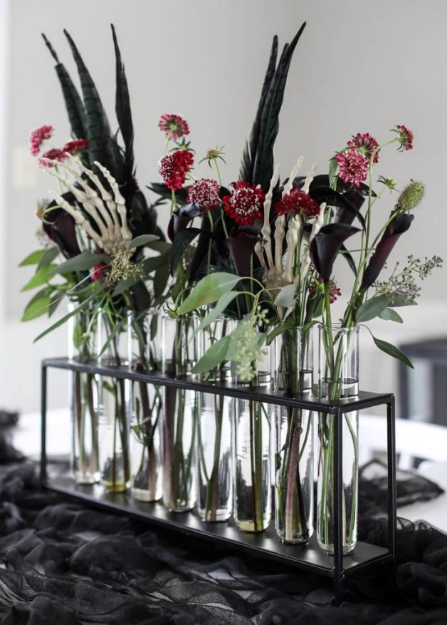 a gorgeous Halloween floral arrangement of red, pink and deep purple blooms, greenery, feathers and skeleton hands