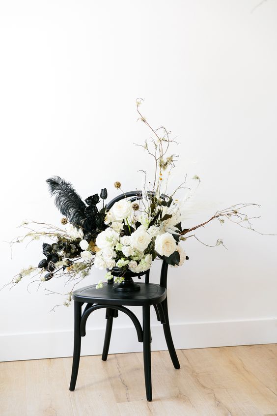 a lovely Halloween flower arrangement with white and black blooms, gilded leaves, seed pods, feathers and some twigs
