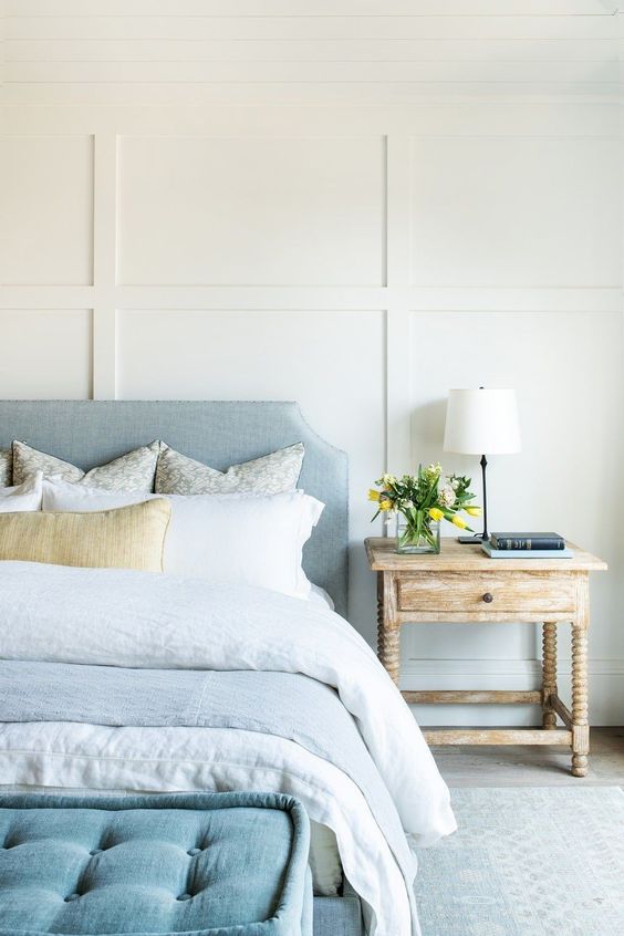 a-lovely-coastal-bedroom-with-paneled-walls-a-pastel-blue-bed-and-neutral-bedding-a-blue-ottoman-and-a-shabby-chic-nightstand.jpg