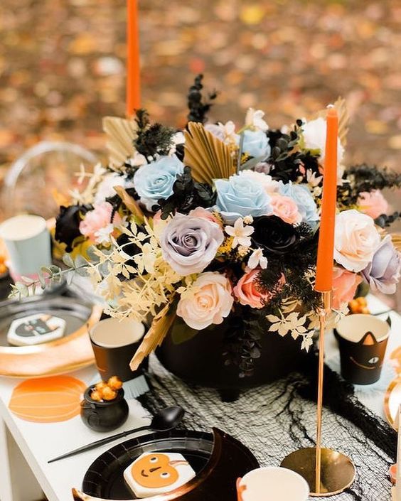 a lovely pastel Halloween arrangement of lilac, blue and pink roses, gilded fronds and leaves plus black touches