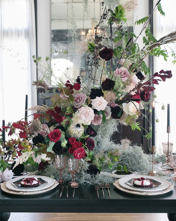 a lush and dimensional Halloween centerpiece of blush, mauve and fuchsia blooms, branches and greenery