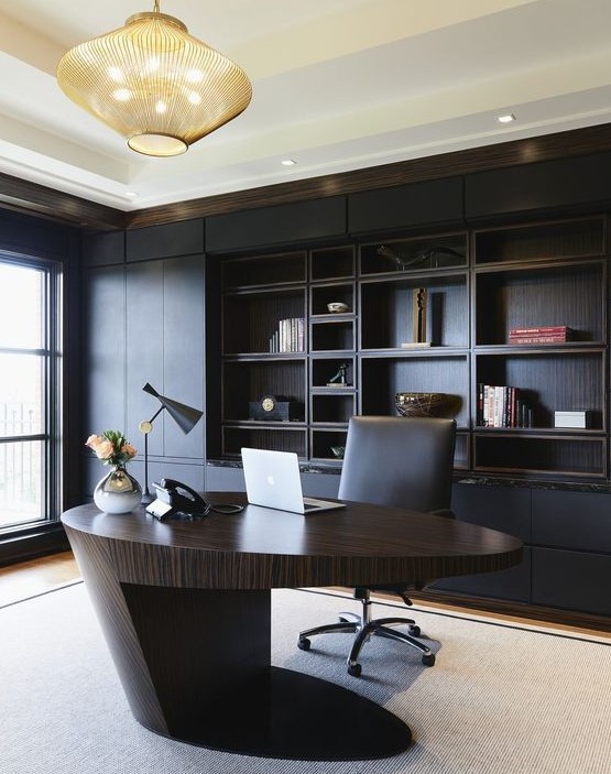 a minimalist and refined home office with a black built-in shelving unit, a sculptural oval desk of rich stained wood, a bold chandelier