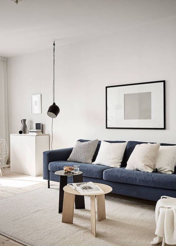 a minimalist meets Scandinavian living room in neutrals, with a navy sofa, neutral pillows, a black pendant lamp and coffee tables