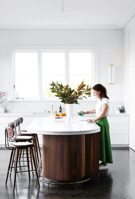 a minimalist white kitchen with sleek cabinets, a fluted curved kitchen island, tall stools and cool lamps