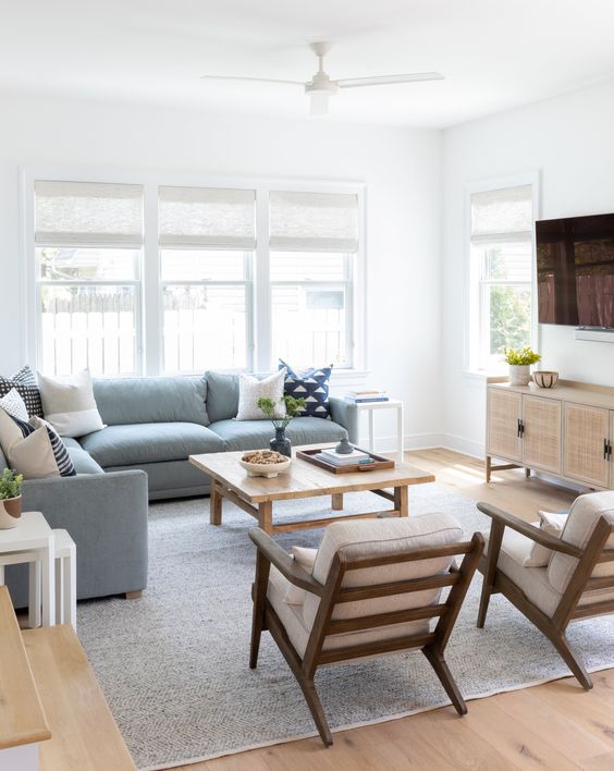 a modern beach living room with a blue sectional and printed pillows, a coffee table and neutral chairs, a cane sideboard