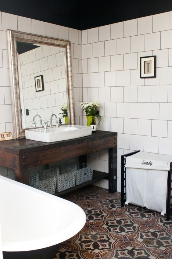 a modern boho bathroom with a dark-stained vanity and a sink, a black clawfoot tub and a printed tile floor