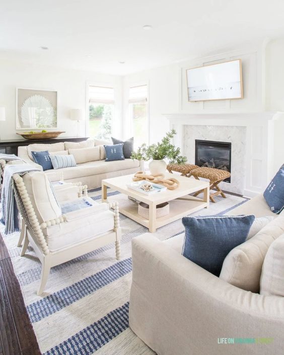 a modern coastal living room with a built-in fireplace, a coffee table, neutral seating furniture, blue pillows, a printed rug