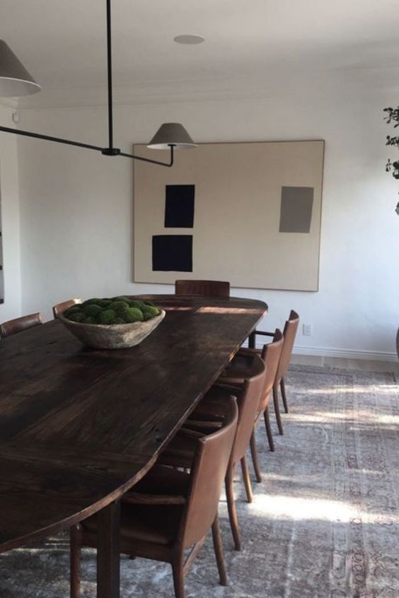 a modern dining room with a dark-stained oval table, brown leather chairs, an abstract artwork and a modern chandelier