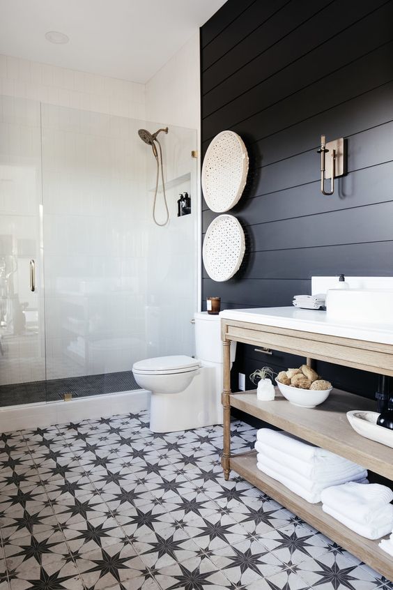 a modern farmhouse bedroom with soot shiplap walls, a shower space, a light-stained vanity, a black and white star tile floor