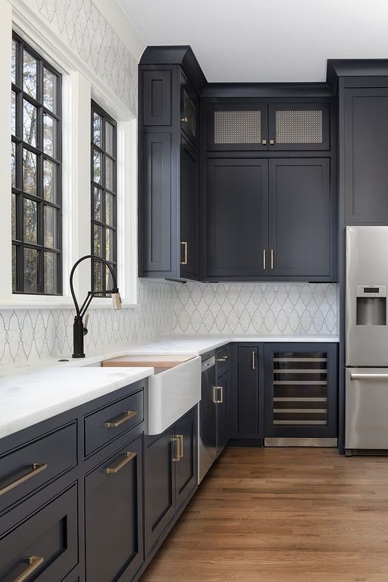 a modern farmhouse kitchen with soot cabinets, a white tile backsplash and white stone countertops, brass handles