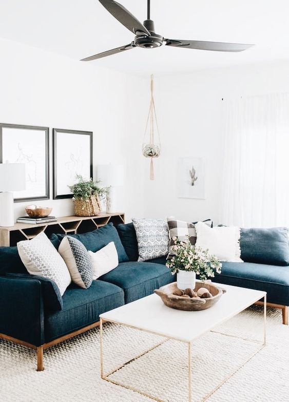 a modern farmhouse living room with a navy sectional, a sideboard, a coffee table, some art and potted blooms and greenery