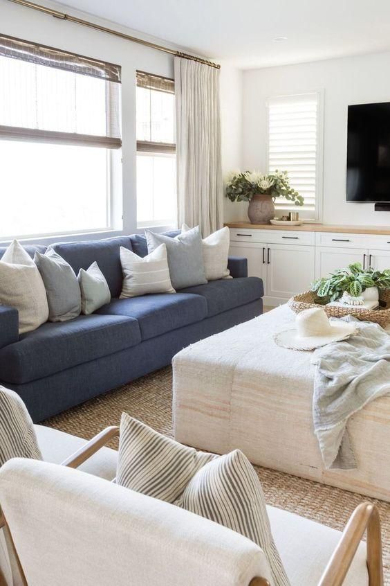 a modern farmhouse living room with built-in cabinets, a blue sofa, a neutral ottoman, neutral chairs, a jute rug and some greenery