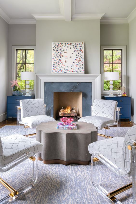 a modern living room with a fireplace clad with marble, blue sideboards, a quirky-shaped coffee table, white and acrylic chairs