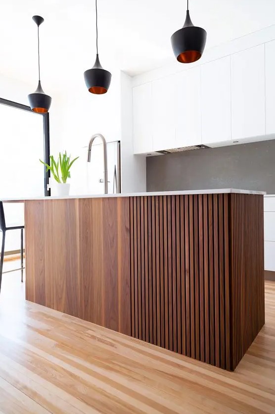 a modern white kitchen with a grey backsplash, a dark-stained slat kitchen island and black pendant lamps is a stylish space